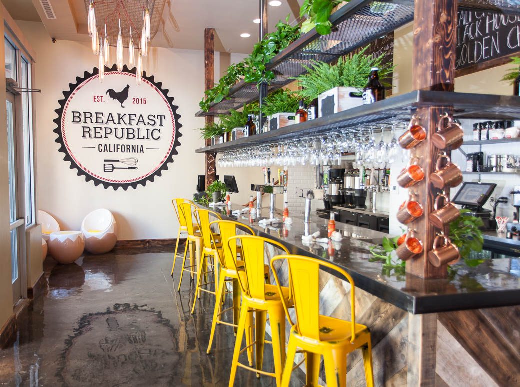 Bright cafe interior with yellow chairs and greenery.